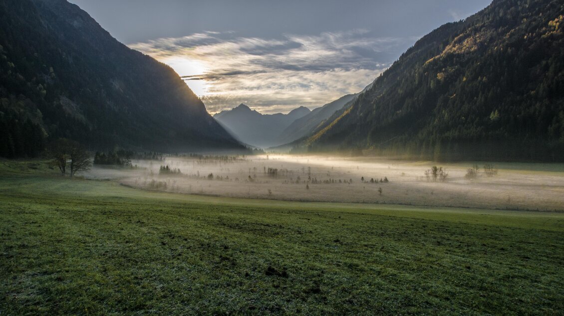 Eine malerische Berglandschaft mit nebelbedecktem Tal und sanften Hügeln. Die Sonne geht am Horizont auf und taucht die Szene in sanftes Licht. | © Gerhard Pilz