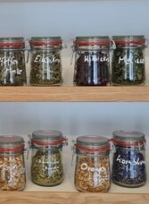 A wooden shelf with several jars containing various spices and herbs. Each jar is labeled and displays a colorful variety of contents. | © The Ginery