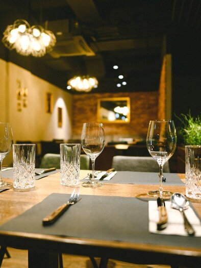 Ein eleganter Tisch in einem Restaurant mit Gläsern und Besteck. Im Hintergrund sind sanfte Lichter und eine stilvolle Inneneinrichtung zu sehen. | © The Kitchen