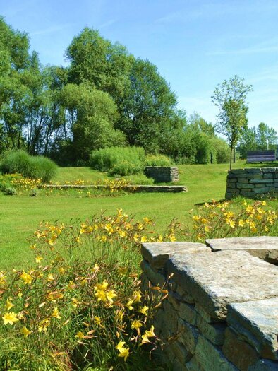 Eine grüne Wiese mit bunten Blumen und verstreuten Steinmauern. Im Hintergrund sind hohe Bäume und ein blauer Himmel zu sehen. | © Kurkommission Bad Blumau