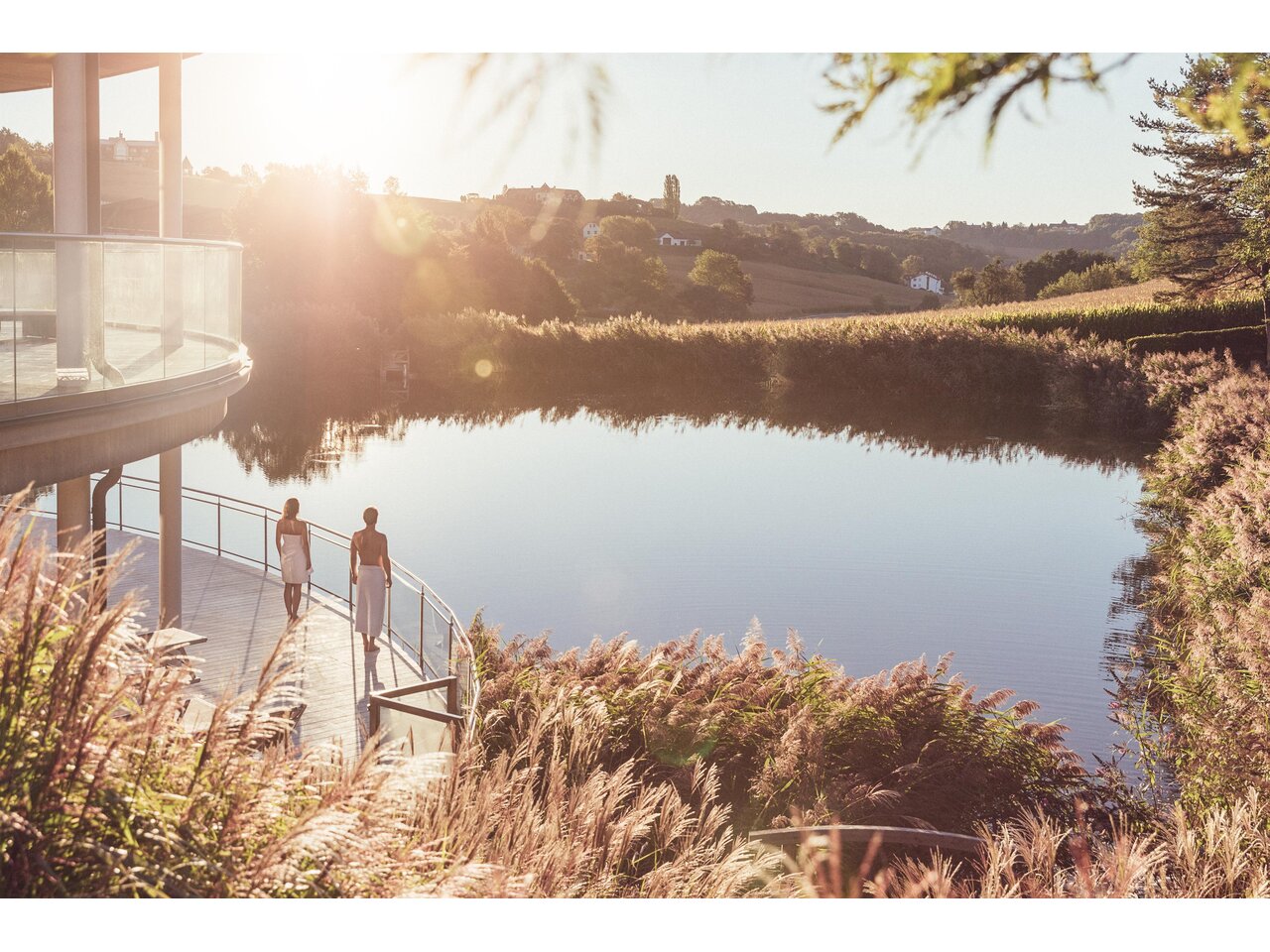 <p>Eine ruhige Seenlandschaft bei Sonnenuntergang. Zwei Personen spazieren entlang der Uferpromenade. Thermenresort Loipersdorf in Bad Loipersdorf.</p> | © TRL