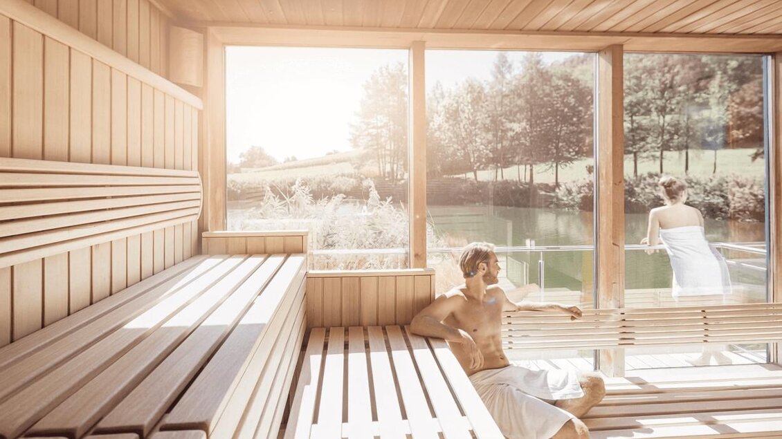<p>Ein entspannender Saunaraum mit Holzwänden und großen Fenstern. Im Vordergrund sitzt ein Mann, während im Hintergrund eine Frau das Panorama genießt. Thermenresort Loipersdorf in Bad Loipersdorf.</p> | © TRL