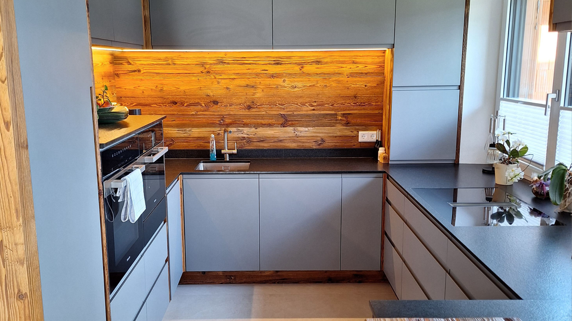 Eine moderne Küche mit einem hellen Holzschrank und einer dunklen Arbeitsplatte. Der Raum wirkt schlicht und funktional. | © Tischlerei Egger