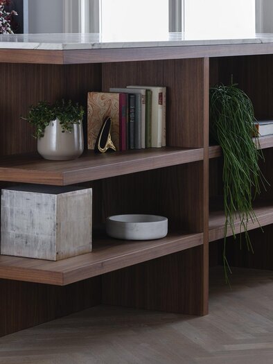 A modernly designed table with open shelves made of wood. On the shelves, there are plants, books, and decorative objects. | © Daniela Trost