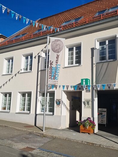 Ein Gebäude mit bunten Fahnen und einem einladenden Eingang. Die Fassade ist hell und freundlich, umgeben von einem klaren blauen Himmel. | © Tanja Beren