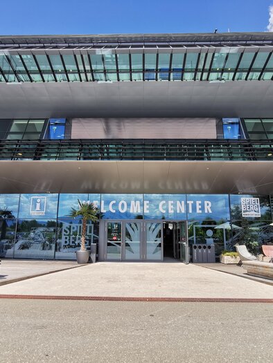 Ein modernes Gebäude mit der Aufschrift "WELCOME CENTER". Vor dem Eingang stehen Pflanzen und ein Tisch mit Sonnenschirm. | © Patrizia Schreibmayr