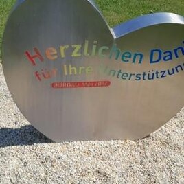 Ein herzförmiges Schild aus Metall steht auf einem Kiesboden. Es bedankt sich mit bunten Buchstaben für die Unterstützung. | © Gemeinde Burgau