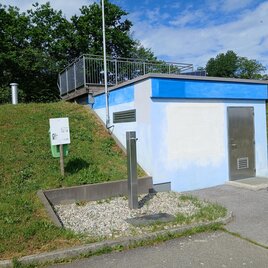 Ein kleiner, blau-weißer Gebäudekomplex steht auf einem Hügel, umgeben von grünem Gras. Am Gebäude befindet sich ein Zugang und eine Treppe, die zu einer Plattform führt. | © Helmut Sommer