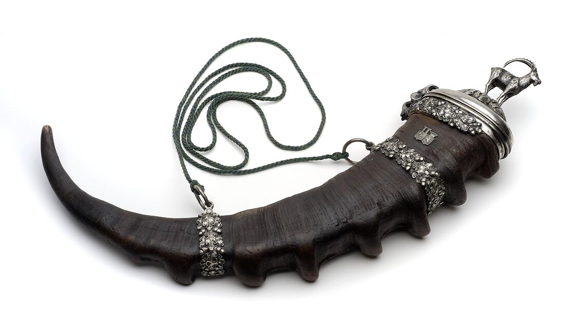 Ein dekorierter Trinkhorn mit Verzierungen aus Metall und einer Schnur. Das Horn hat eine geschwungene Form und ist kunstvoll gestaltet. | © Universalmuseum Joanneum - N. Lackner