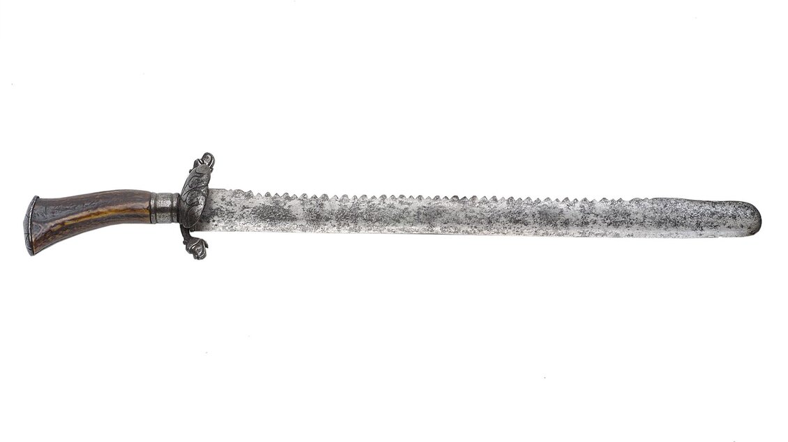 Ein langer, rustikaler Säbel mit einem verzierten Griff. Die Klinge hat eine gezahnter Kante und eine interessante, strukturierte Oberfläche. | © Universalmuseum Joanneum - N. Lackner