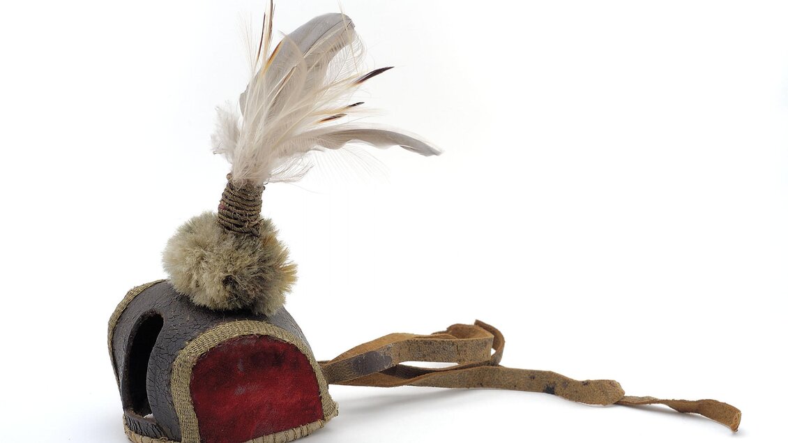 Ein historischer Helm mit einem dekorativen Federbesatz und einer roten Unterseite. Der Helm hat auch einen langen Lederband zum Tragen. | © Universalmuseum Joanneum - N. Lackner