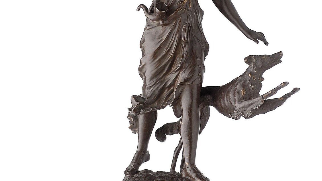 Eine bronzene Statue einer Jagdgöttin, die mit einem Speer in der Hand steht. Ein Hund läuft neben ihr auf einem schwarzen Sockel. | © Universalmuseum Joanneum - N. Lackner