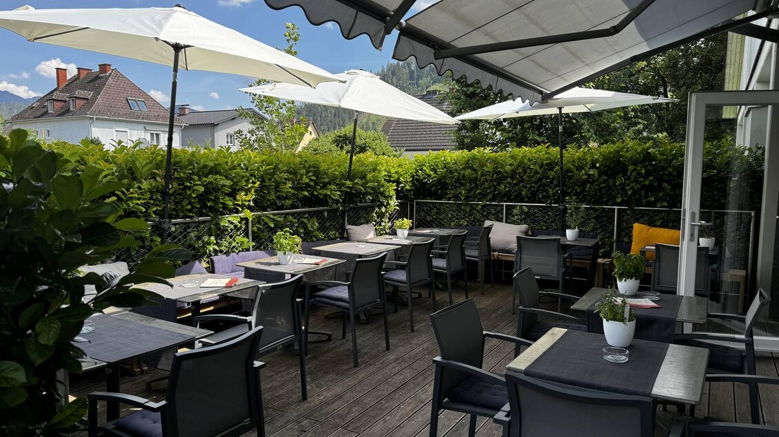 Eine gemütliche Terrasse mit Sonnenschirmen und Tischen. Umgeben von grünen Pflanzen, ideal für draußen essen und entspannen. | © Unser Cafe'