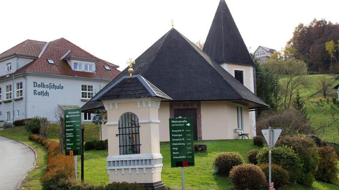 Ein charmantes, kleines Gebäude mit einem scharfen Dach steht an einer Straße. Nebenan befindet sich ein größeres Gebäude mit der Aufschrift "Dolkalschule Retten." | © TV Südsteiermark