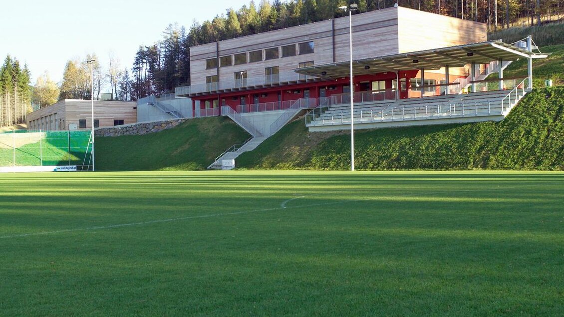 Ein Sportplatz mit grünem Rasen und einem modernen Gebäude im Hintergrund. Das Gelände ist von Bäumen umgeben und bietet Platz für Sportaktivitäten. | © Gemeinde Pöllauberg