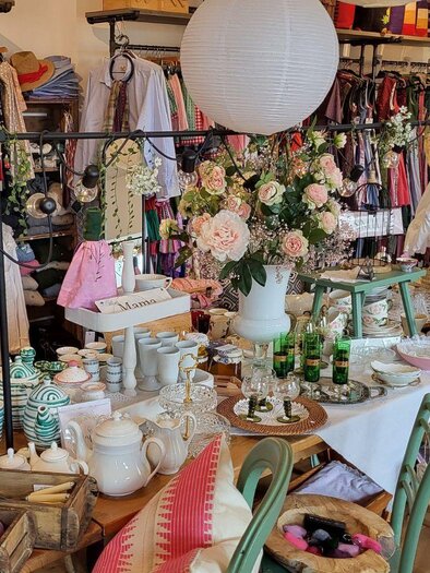 An inviting store with colorful garments and many decorative items. On a table, dishes, flowers, and various accessories are beautifully arranged. | © Petra Kirchschlager