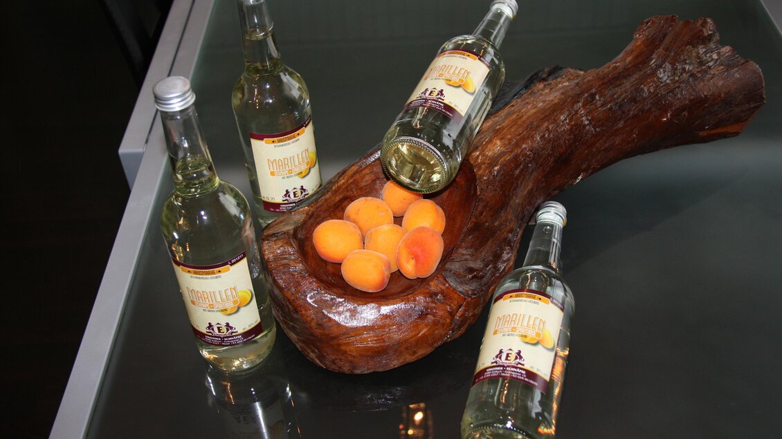Flaschen mit Edelbränden und frischen Marillen auf einem dekorativen Holzstück in der Vinothek Ellersdorfer in Köflach. | © Ellersdorfer