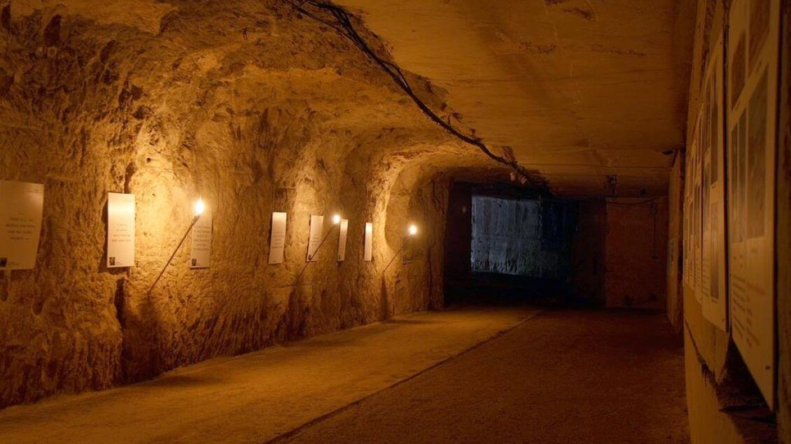 Ein unterirdischer Tunnel mit beleuchteten Wänden und Informationen an der Seite. Der Boden ist eben und das Licht schafft eine ruhige Atmosphäre. | © Stefan Matic