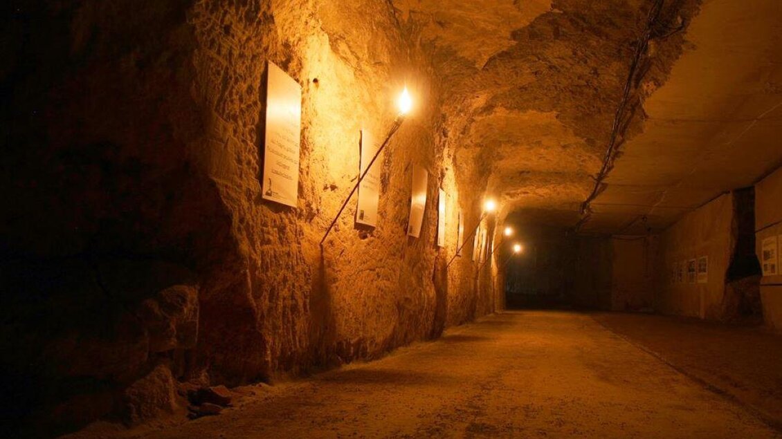 Ein schmaler, beleuchteter Gang in einer Höhle mit rauen Wänden. An der Wand hängen einige Schilder, die Informationen bieten. | © Stefan Matic