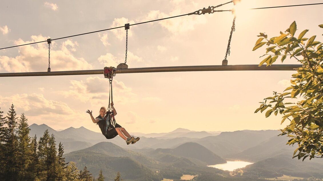 Eine Person schwebt mit einer Zipline über eine wunderschöne Berglandschaft. Die Sonne scheint und die Natur ist grün und beruhigend. | © Mariazeller Bürgeralpe