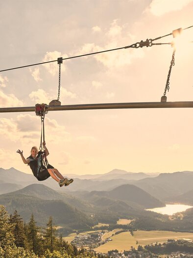 Eine Person schwebt mit einer Zipline über eine wunderschöne Berglandschaft. Die Sonne scheint und die Natur ist grün und beruhigend. | © Mariazeller Bürgeralpe