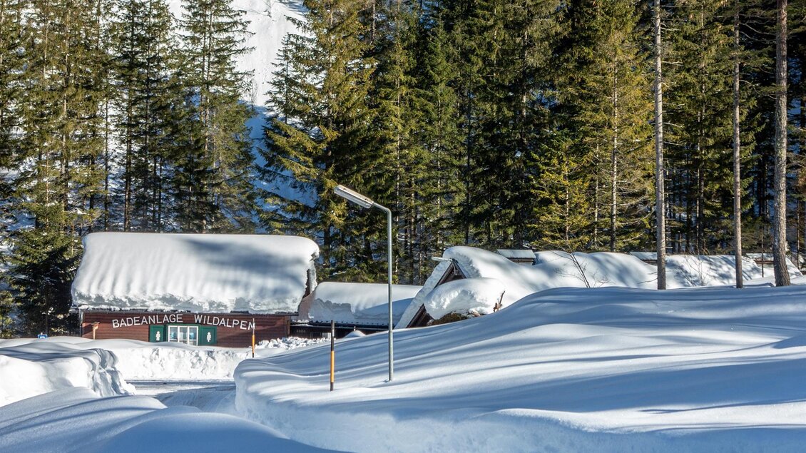 Eine verschneite Landschaft mit Hütten und hohen, grünen Bäumen. Der Himmel ist klar und die Sonne scheint auf die weiße Schneedecke. | © Christian Scheucher