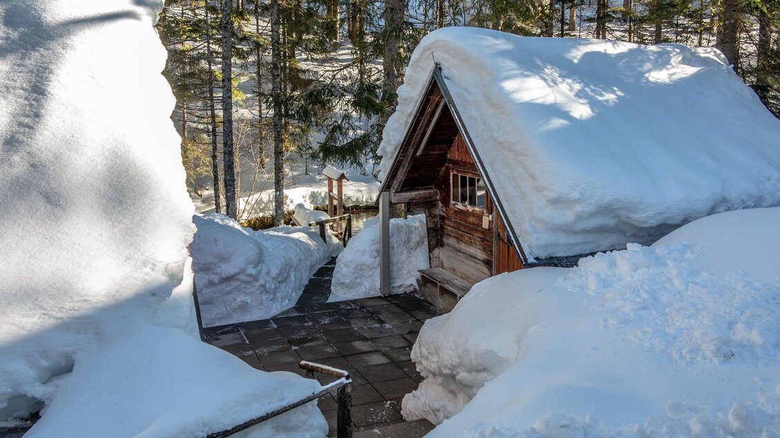 Eine charmante Hütte im Schnee, umgeben von hohen Bäumen. Der Schnee liegt dick auf dem Dach und dem Boden. | © Christian Scheucher