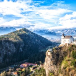 A breathtaking landscape with mountains in the background and a small church on a hill. The sky is clear and nature is green and vibrant. | © Franz Jöbstl