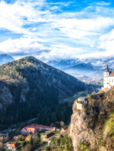 Eine atemberaubende Landschaft mit Bergen im Hintergrund und einer kleinen Kirche auf einem Hügel. Der Himmel ist klar und die Natur ist grün und lebendig. | © Franz Jöbstl