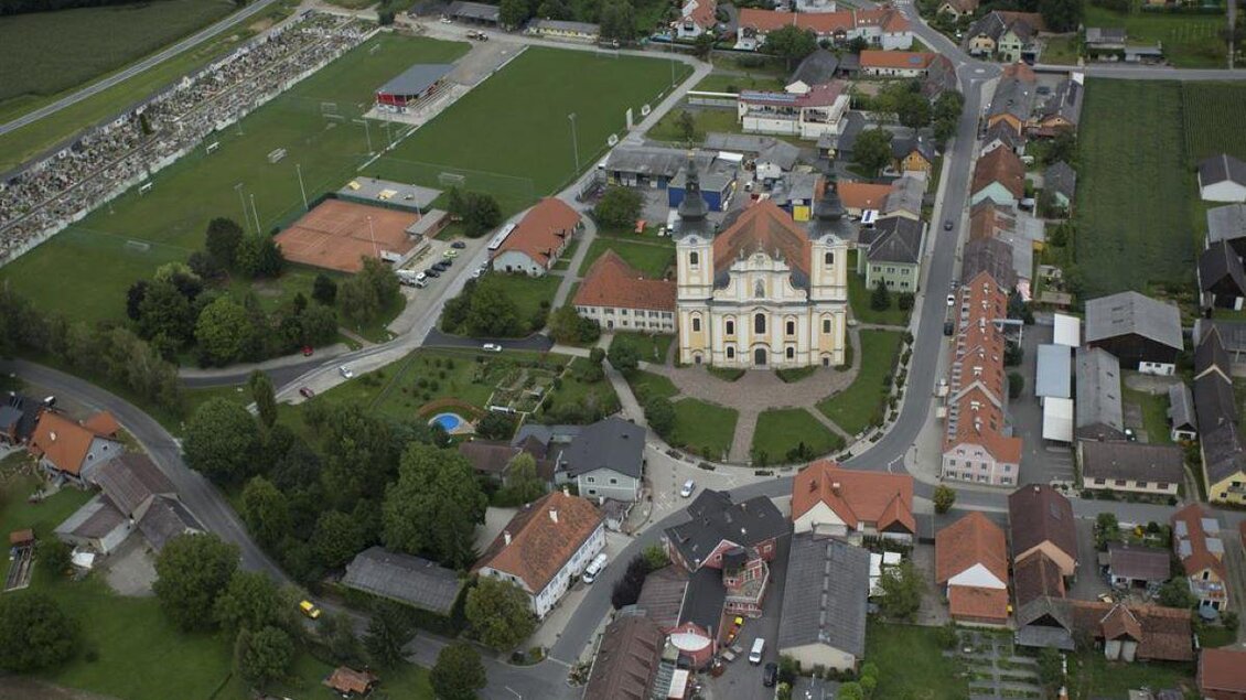 Eine Luftaufnahme einer kleinen Stadt mit einem beeindruckenden Gebäude im Zentrum. Umgeben von grünen Feldern und kleinen Wohnhäusern. | © Andreas Ruckenstuhl