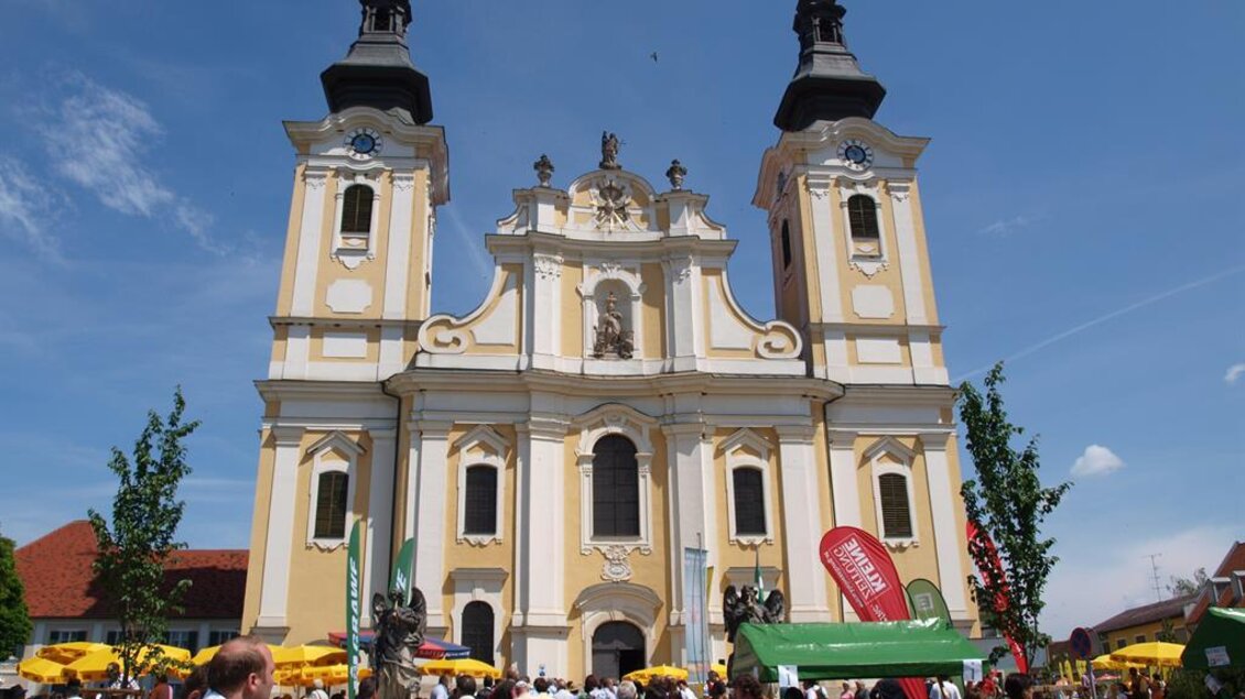 Eine prächtige Kirche mit zwei Türmen und gelber Fassade. Viele Menschen versammeln sich davor, während Festlichkeiten stattfinden. | © Andreas Ruckenstuhl