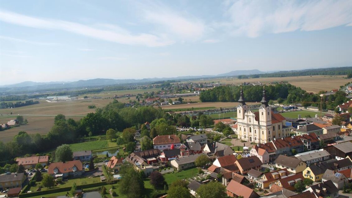 Eine malerische Stadt mit einer Kirche im Hintergrund, umgeben von grünen Feldern und Hügeln. Die Dächer der Häuser sind in verschiedenen Farben und die Landschaft ist friedlich und einladend. | © Andreas Ruckenstuhl