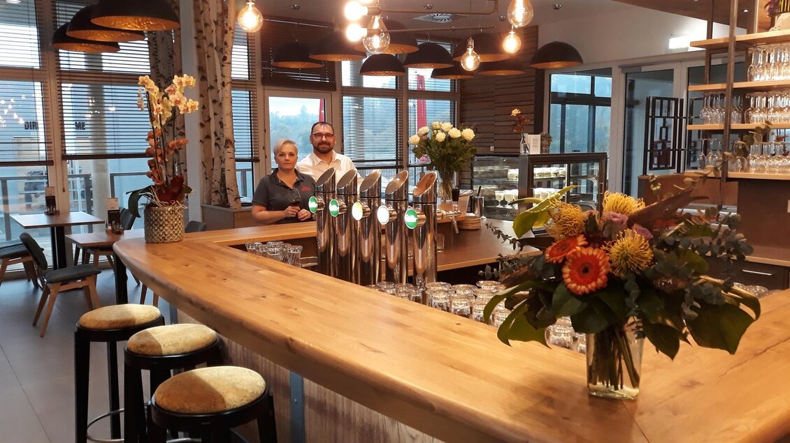 Die Gastgeber im Walter's Genusswirt in Voitsberg stehen hinter der Bar und begrüßen die Gäste in einem warmen, einladenden Ambiente. Die moderne Einrichtung und florale Dekoration sorgen für eine gemütliche Atmosphäre. | © TV Lipizzanerheimat