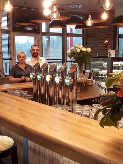 Die Gastgeber im Walter's Genusswirt in Voitsberg stehen hinter der Bar und begrüßen die Gäste in einem warmen, einladenden Ambiente. Die moderne Einrichtung und florale Dekoration sorgen für eine gemütliche Atmosphäre. | © TV Lipizzanerheimat