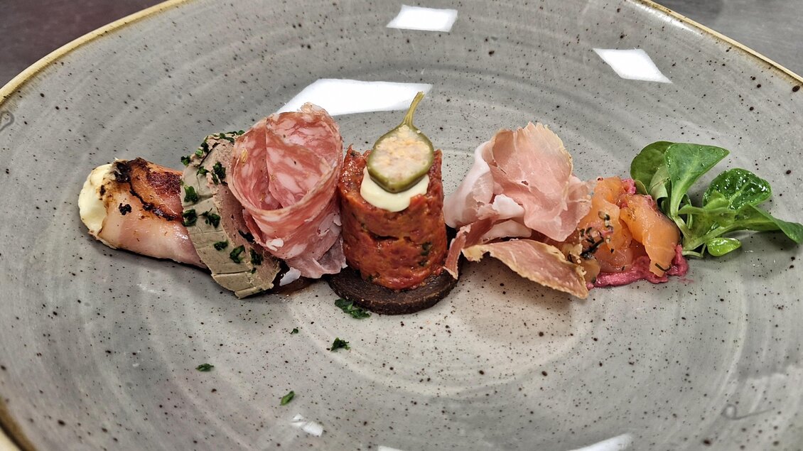 Kreative Vorspeise im Walter's Genusswirt in Voitsberg: Eine Auswahl an feinstem Schinken, Wurst und Leberpastete, serviert mit frischem Brot und Kräutern. | © Walter Prettenthaler
