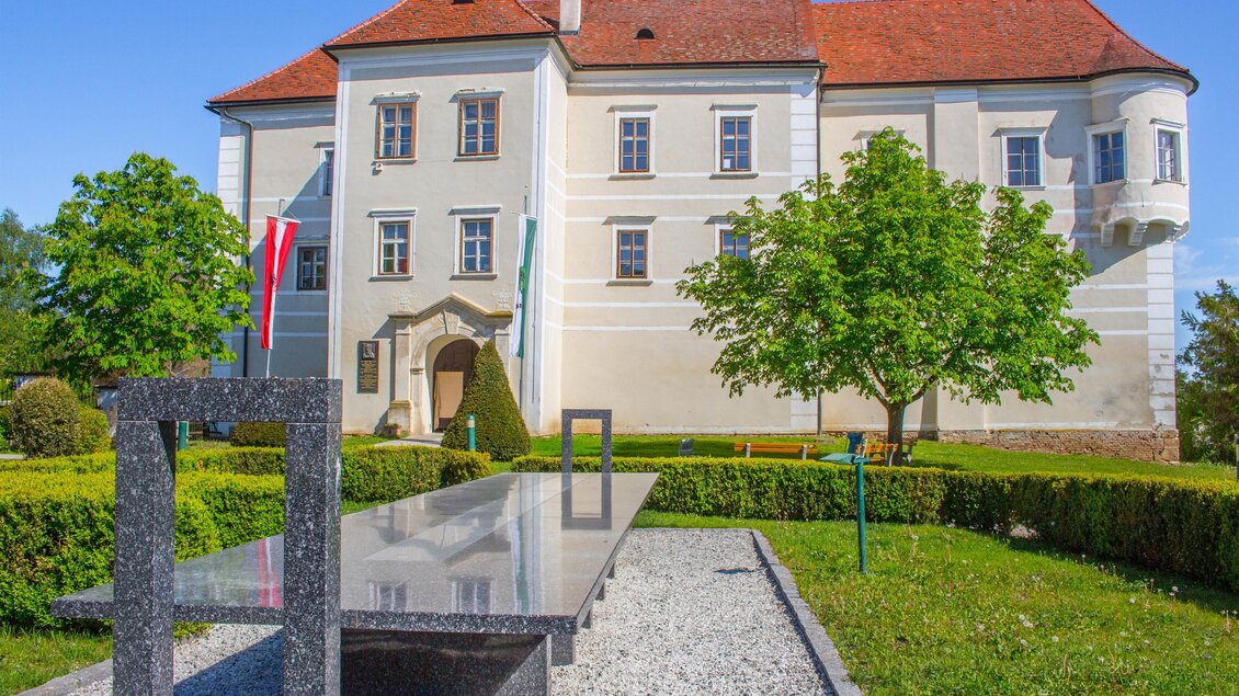 Ein historisches Gebäude mit einem roten Satteldach und schönen Fenstern. Im Vordergrund befindet sich eine moderne Steininstallation in einem gepflegten Garten. | © Sandra Brünner