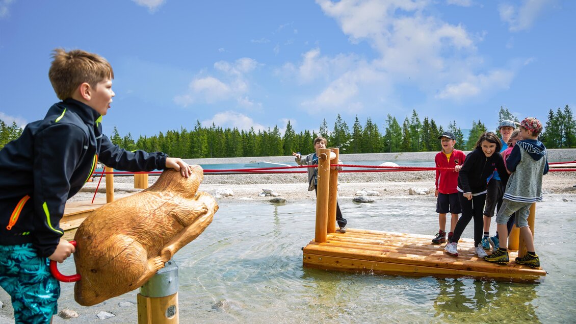 Kinder spielen an einem Wasser-Spielplatz. Einige stehen auf einer Holzplattform, während ein anderes Kind ein Spielzeug bedient. | © TV Hochsteiermark | Fred Lindmoser