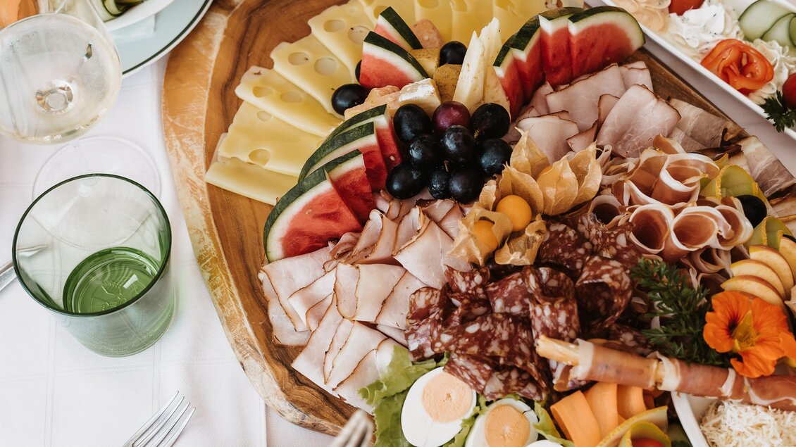 Ein schön angerichteter Teller mit verschiedenen Käsesorten, Wurst und frischem Obst. Gläser und Teller sind liebevoll dekoriert, was die Tafel einladend wirken lässt. | © MichaelaLorber