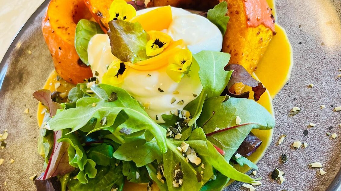 Ein schön angerichteter Teller mit gebackenem Kürbis, einem pochierten Ei und frischem Salat. Die Farben sind lebendig und die Präsentation ist sehr appetitlich. | © Michaela Lorber