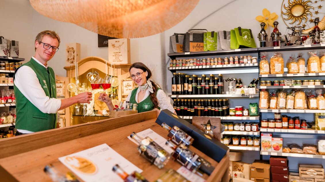 <p>Zwei Mitarbeiter präsentieren Produkte im 24-Stunden-Genussladen im Weingut Destillerie Da Finz in Mooskirchen.</p> | © Region Graz - Mias Photoart