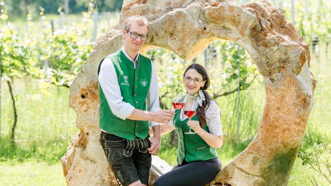 Zwei Personen genießen ein Glas Schilcherwein vor einer Steinskulptur in Herzform  im Weingut Destillerie Da Finz in Mooskirchen. | © Region Graz - Mias Photoart