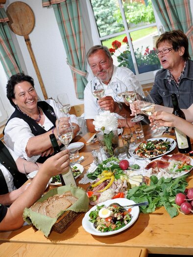 A cheerful gathering of people at a festive meal. They toast with glasses and enjoy various dishes on the table. | © Weingut Gerngross
