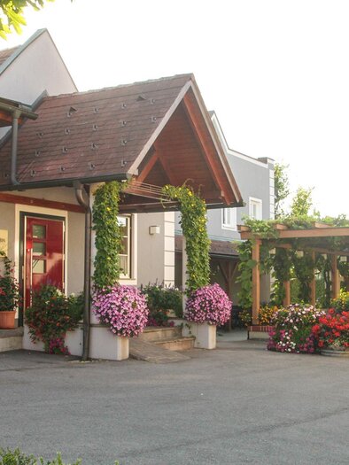 An inviting building with blooming plants and a shaded outdoor area. The atmosphere is friendly and welcoming. | © Weingut Grabin