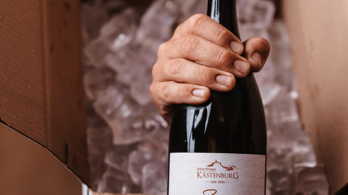 Eine Hand hält eine Flasche Roséwein aus einer geöffneten Kartonbox. Die Box ist mit Eis gefüllt. | © Genuss-Geschwister Kästenburg