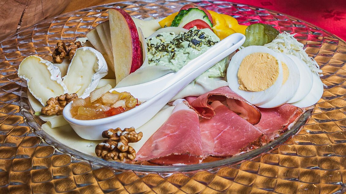 Ein Teller mit einer Auswahl an Wurst, Käse, gekochtem Ei und frischen Früchten. Dazu gibt es eine Schale mit Chutney und einige Walnüsse. | © Weingut Pölzl
