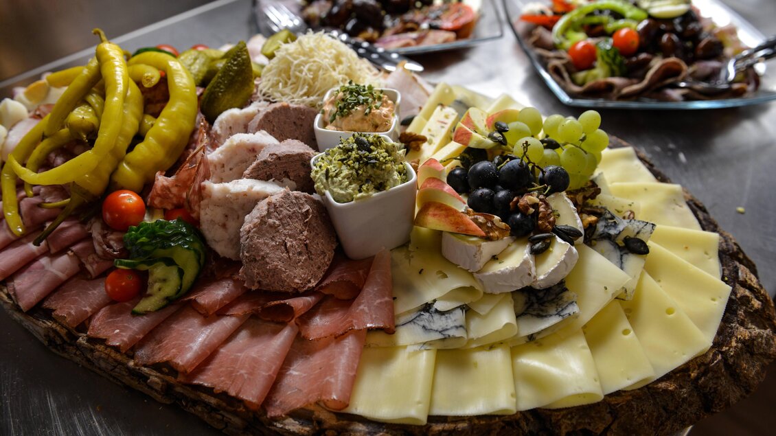 Eine köstliche Platte mit Wurst, Käse, Trauben und verschiedenen Beilagen. Im Hintergrund sind weitere Salate und Snacks zu sehen. | © Weingut & Buschenschank Pölzl