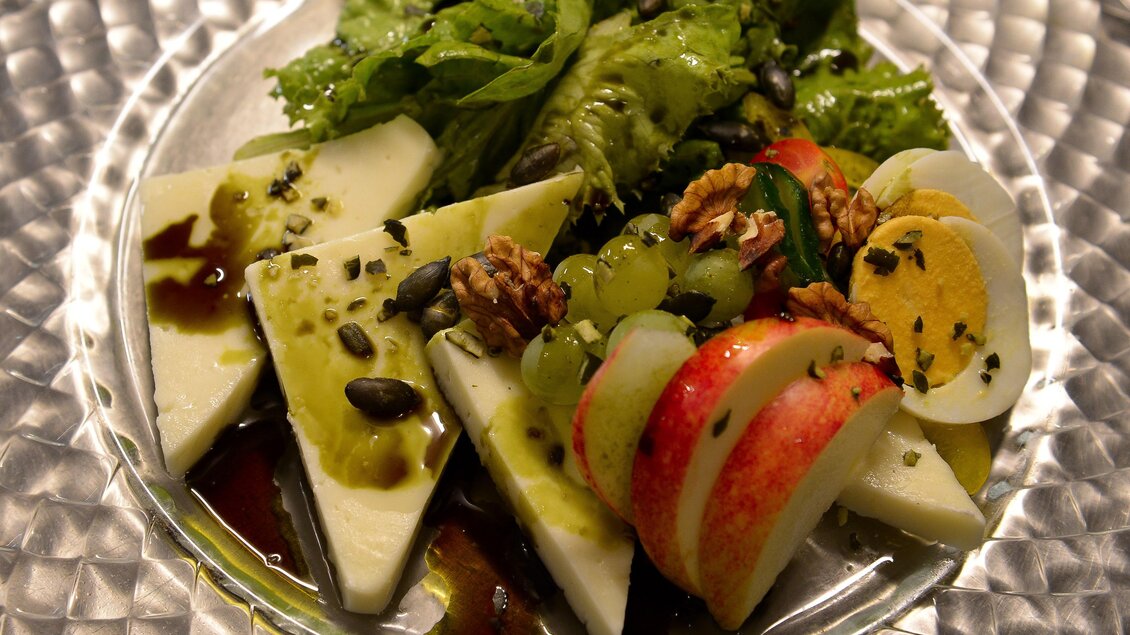 Ein frischer Salat auf einem eleganten Glasplateau. Er besteht aus grüner Salat, Äpfeln, Trauben und kernigen Toppings. | © Weingut & Buschenschank Pölzl