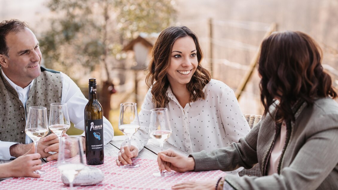 Eine Gruppe von Freunden sitzt an einem Tisch und genießt ein Glas Wein. Sie lachen und unterhalten sich in einer entspannten Atmosphäre im Freien. | © Michaela Lorber