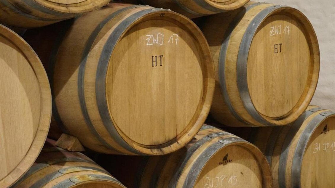 Eine Reihenfolge von Holzfässern lagert aufeinander. Die Fässer sind mit Markierungen versehen und zeigen eine rustikale Weinkeller-Atmosphäre. | © Weingut Perner