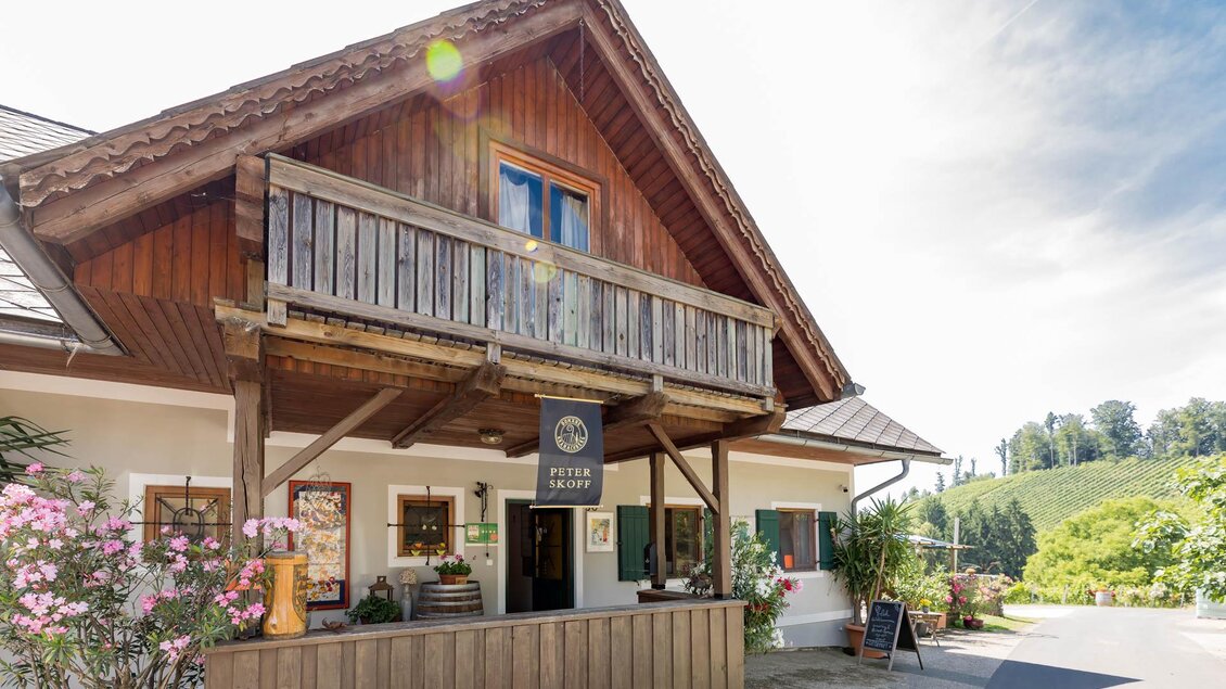 Ein rustikales Restaurant mit Holzfassade und Balkon. Blumen und grüne Landschaft umgeben das Gebäude.